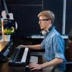 Młody mężczyzna deejay w dżinsowej koszuli patrząc na miksowanie dźwięku na ekranie komputera, siedząc przy biurku przed monitorem