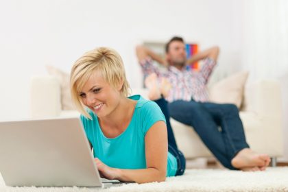 Piękna kobieta, leżąc na dywanie i za pomocą laptopa