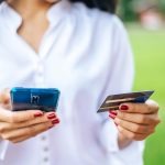 Środkowa sekcja kobiety używającej telefonu komórkowego podczas trzymania karty kredytowej na zewnątrz