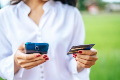 Środkowa sekcja kobiety używającej telefonu komórkowego podczas trzymania karty kredytowej na zewnątrz