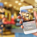 Zbliżenie ręki trzymającej smartfon przeciwko oświetlonym światłom