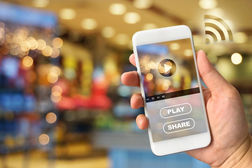 Zbliżenie ręki trzymającej smartfon przeciwko oświetlonym światłom