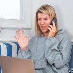 Dziewczyna rozmawiająca przez telefon i używająca laptopa w pobliżu okna w domu