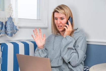 Dziewczyna rozmawiająca przez telefon i używająca laptopa w pobliżu okna w domu