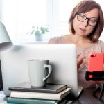 Wykwalifikowana kobieta w średnim wieku komunikująca się online lub studiująca na odległość przez telefon na statywie,
