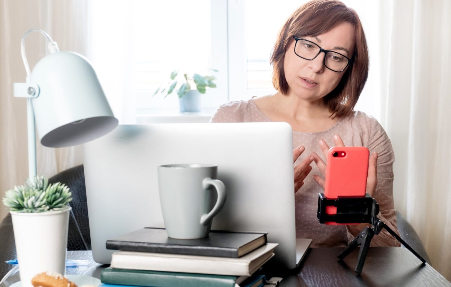 Wykwalifikowana kobieta w średnim wieku komunikująca się online lub studiująca na odległość przez telefon na statywie,