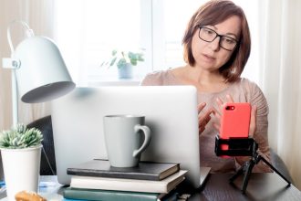 Wykwalifikowana kobieta w średnim wieku komunikująca się online lub studiująca na odległość przez telefon na statywie,