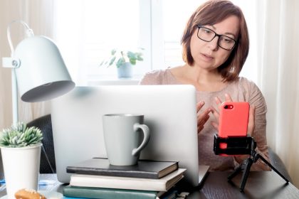 Wykwalifikowana kobieta w średnim wieku komunikująca się online lub studiująca na odległość przez telefon na statywie,