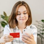 Młoda kobieta robi zakupy online za pomocą karty kredytowej za pomocą smartfona w domu w pomieszczeniach