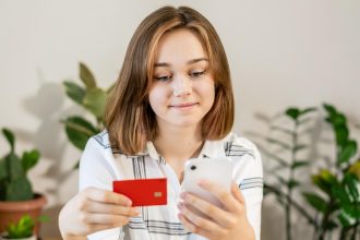 Młoda kobieta robi zakupy online za pomocą karty kredytowej za pomocą smartfona w domu w pomieszczeniach