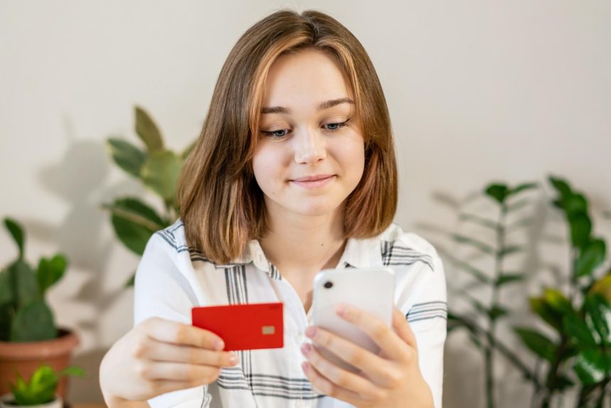 Młoda kobieta robi zakupy online za pomocą karty kredytowej za pomocą smartfona w domu w pomieszczeniach