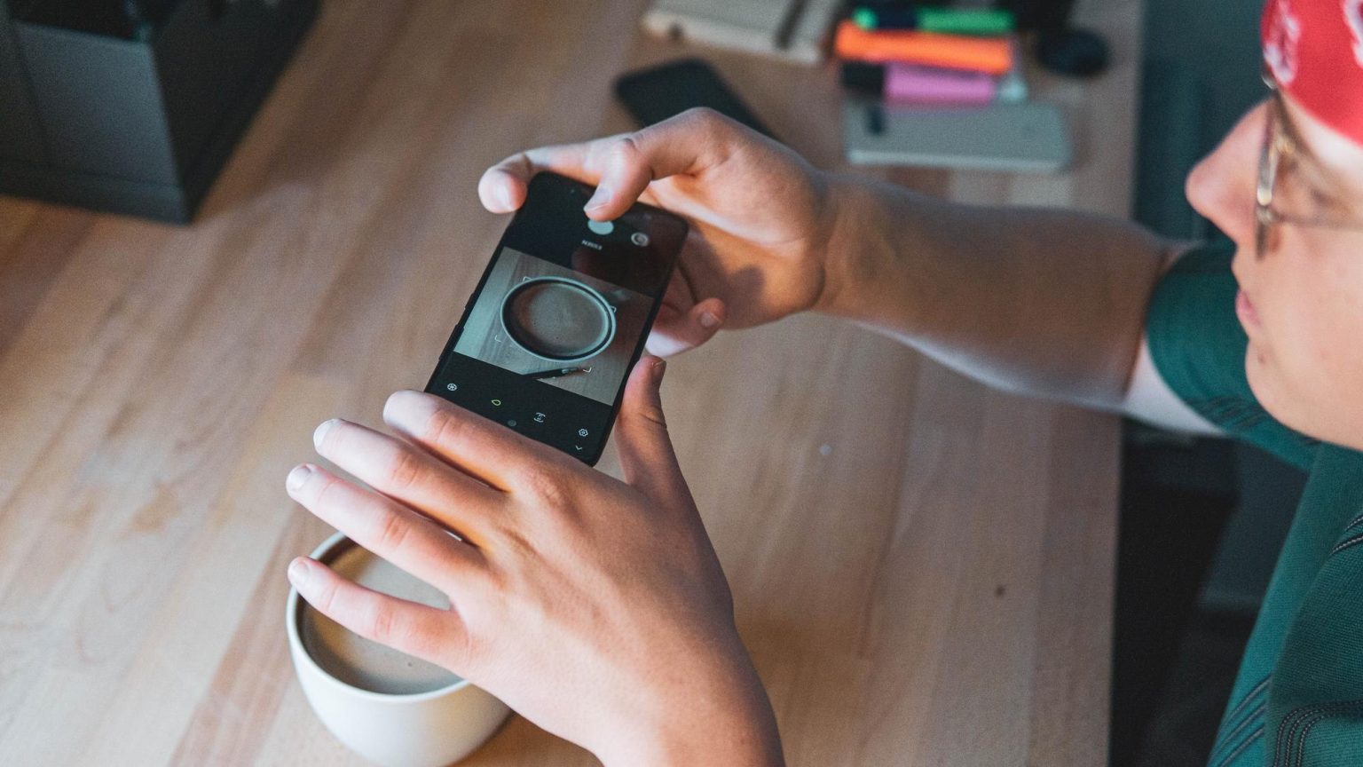 Środkowa część kobiety fotografującej ze smartfonem na stole