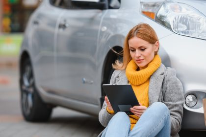 Kobieta w pobliżu wypożyczonego samochodu elektrycznego. Pojazd ładowany na stacji ładowania.
