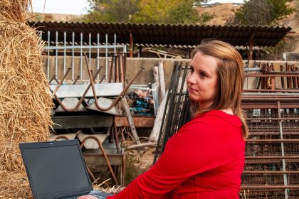 Młoda kobieta używająca laptopa na balie siana na farmie