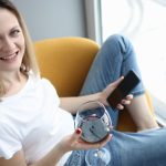 Młoda kobieta siedzi na fotelu przy lampce czerwonego wina i telefonu