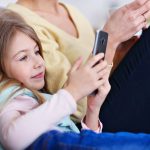 młoda mama i jej córeczka używają smartfona i siedzą na kanapie w domu