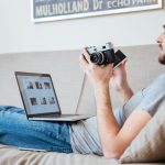 Skoncentrowany, atrakcyjny mężczyzna fotograf używający starego zabytkowego frontu i laptopa na kanapie w domu