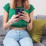 Kobieta przy użyciu telefonu komórkowego, siedząc na kanapie w domu.