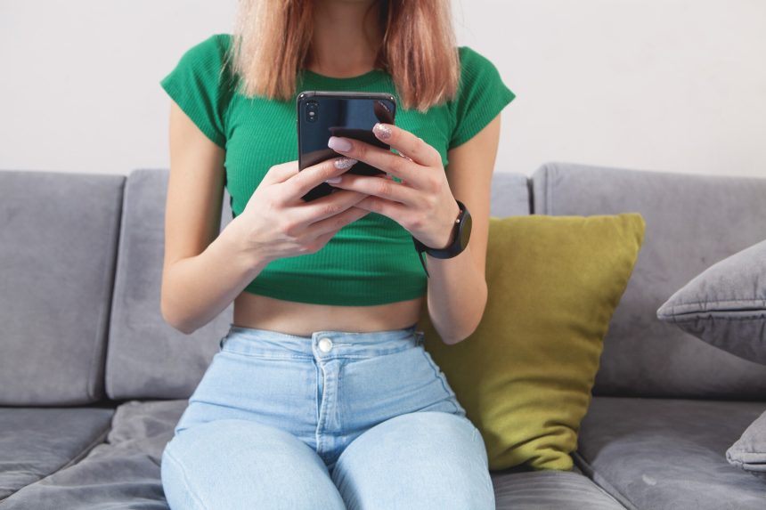 Kobieta przy użyciu telefonu komórkowego, siedząc na kanapie w domu.