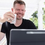 Uśmiechnięty młody człowiek siedzący z filiżanką kawy i pracujący na tablecie na ulicy