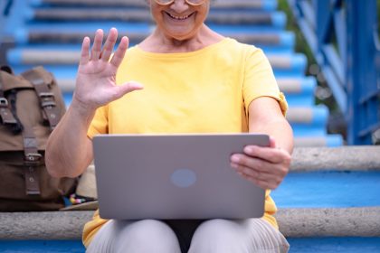 Starsza kobieta siedzi na zewnątrz na schodach w vlog z laptopa. Podróżnik z plecakiem korzystający z technologii