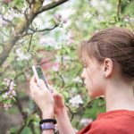 Młoda dziewczyna w kwitnącym ogrodzie robi zdjęcia kwitnących drzew smartfonem