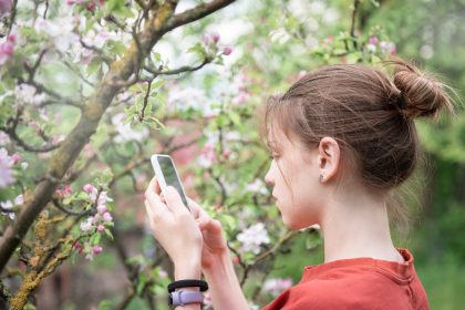 Młoda dziewczyna w kwitnącym ogrodzie robi zdjęcia kwitnących drzew smartfonem