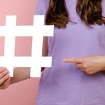 Bliska przycięte młoda kobieta trzyma duży duży biały znak hashtag, wirusowe treści internetowe, promocja w Internecie, na białym tle nad różowym kolorem tła w studio. Koncepcja strategii blogowania blogów