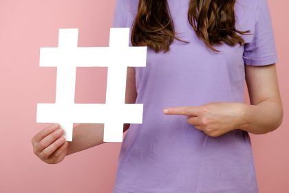 Bliska przycięte młoda kobieta trzyma duży duży biały znak hashtag, wirusowe treści internetowe, promocja w Internecie, na białym tle nad różowym kolorem tła w studio. Koncepcja strategii blogowania blogów
