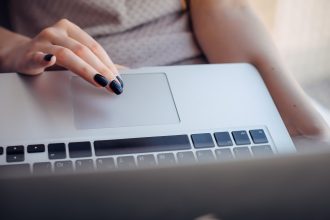 Zbliżenie dłoni młodej kobiety z jasnym manicure na touchpadzie laptopa, Selektywny fokus.
