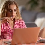 Zniesmaczona blond studentka wygodnie siedzi przy biurku podczas lekcji online w domu z powodu pandemii COVID-19.