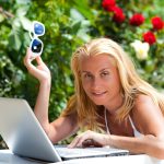 Młoda blond kobieta w białym bikini, leżąc na leżaku z laptopem nad zielonymi roślinami
