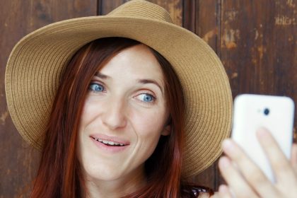Dziewczyna co selfie na zewnątrz. Portret dziewczyny z rudymi włosami z białym telefonem.