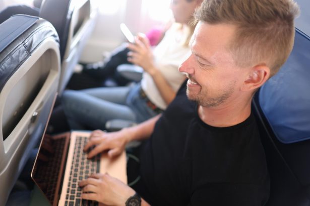 Młody człowiek latający w samolocie i piszący na klawiaturze laptopa