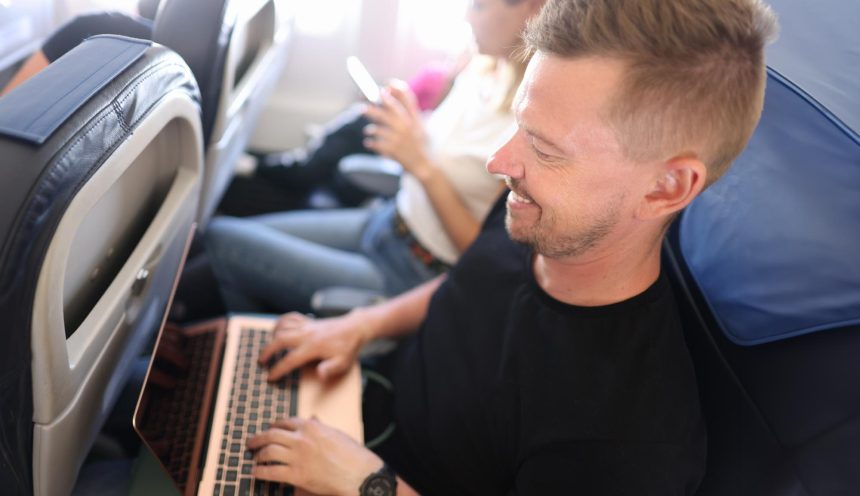 Młody człowiek latający w samolocie i piszący na klawiaturze laptopa