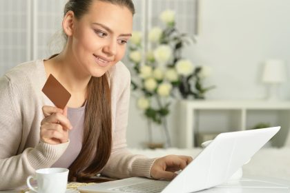 Młoda piękna kobieta z wizytówką za pomocą laptopa, w pomieszczeniu
