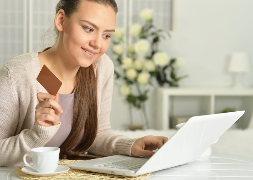 Młoda piękna kobieta z wizytówką za pomocą laptopa, w pomieszczeniu