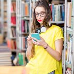 Młody student korzystający ze smartfona w bibliotece