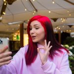 Piękna rudowłosa influencerka blogger dziewczyna w kawiarni rozmawia rozmowy wideo za pomocą smartfona z subskrybentami w sieciach społecznościowych.