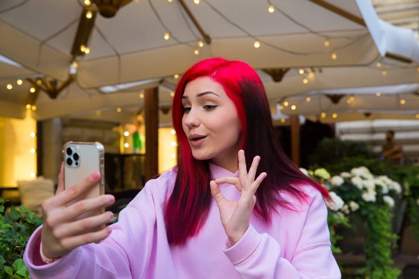 Piękna rudowłosa influencerka blogger dziewczyna w kawiarni rozmawia rozmowy wideo za pomocą smartfona z subskrybentami w sieciach społecznościowych.