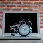 Koncepcja zakupów i sprzedaży detalicznej w Czarny piątek. Wózek na zakupy wózek laptop z zegarem na drewnianym stole z czerwoną ceglaną ścianą. Koncepcja marketingu lub zakupu supermarketu online.
