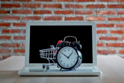 Koncepcja zakupów i sprzedaży detalicznej w Czarny piątek. Wózek na zakupy wózek laptop z zegarem na drewnianym stole z czerwoną ceglaną ścianą. Koncepcja marketingu lub zakupu supermarketu online.
