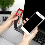 Kobiece dłonie trzymające zegarek monitorujący tętno i smartfon na tle stołu