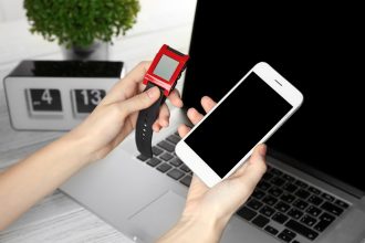 Kobiece dłonie trzymające zegarek monitorujący tętno i smartfon na tle stołu