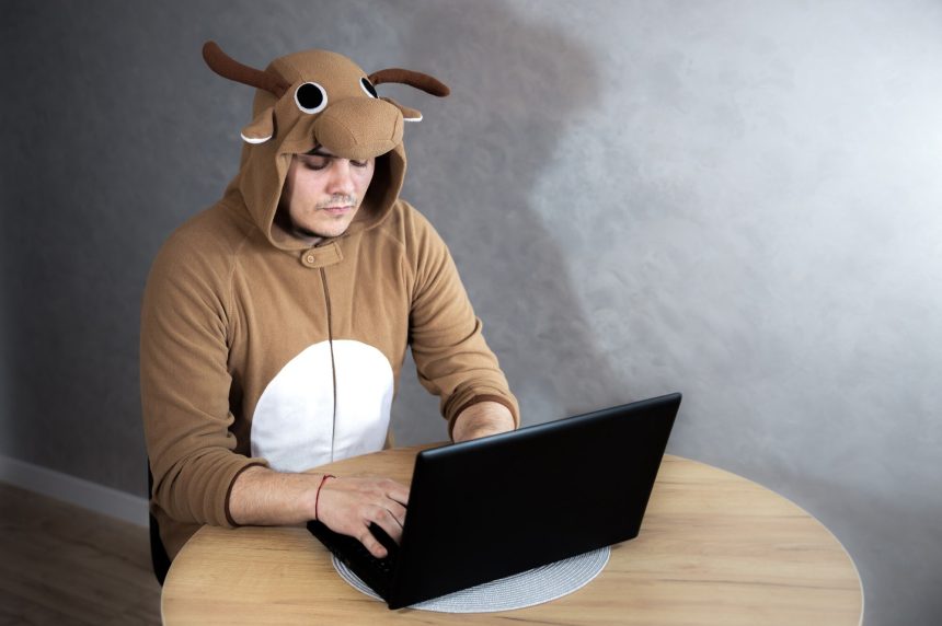 Pracownik biurowy w stroju cosplay krowy. Facet w zabawnej piżamie dla zwierząt w pobliżu laptopa. Mężczyzna pracuje w domu. Szukaj pracy, pojęcie bezrobocia, kryzys gospodarczy. Praca zdalna.