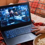 Wyświetlacz laptopa z świątecznym filmem świątecznym „sam w domu” na czerwonej kraciastej kratce w łóżku w domu i kobiecym ręcznym przewijaniem wideo. spędzać czas nadchodząc szczęśliwego nowego roku i wesołych świąt