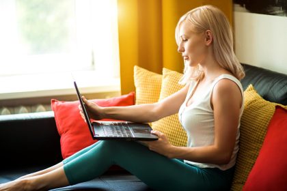 Portret atrakcyjna młoda blondynka bizneswoman nosząca domowe ubrania, pracująca na laptopie w domu, siedząca na wygodnej kanapie w nowoczesnym mieszkaniu. Freelancer, studia, koncepcja pracy zdalnej.