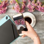 Fotograf Instagram koncepcja warsztatów blogowania, ręka trzyma telefon i robienie zdjęć stylowych kwiatów, filiżankę kawy i tablet graficzny na szarym drewnianym tle rustykalnym. Przestrzeń dla tekstu.