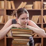 Młoda studentka oparła się o stos książek w bibliotece