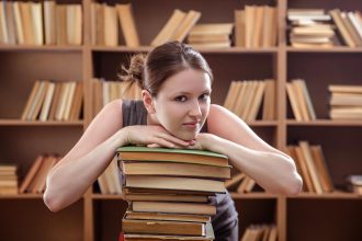 Młoda studentka oparła się o stos książek w bibliotece